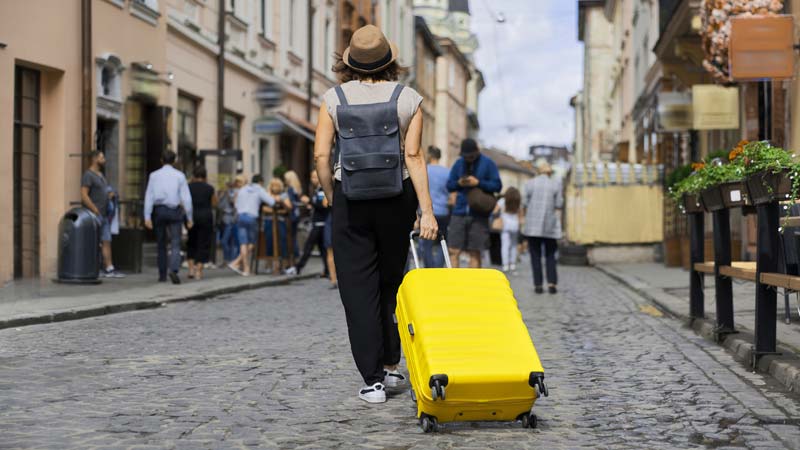 mulher com mala de viagem amarela no centro de uma cidade
